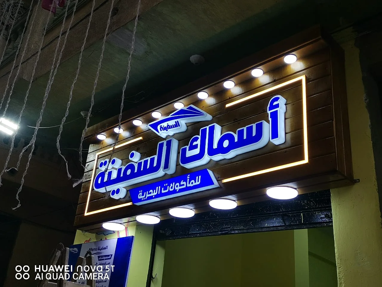 أسماك السفينة — لافتة مطعم على كسوة خشبية بحروف أكريليك مضيئة وإطار إضاءة خطي وسبوتات سفلية. من تنفيذ أبو الخير