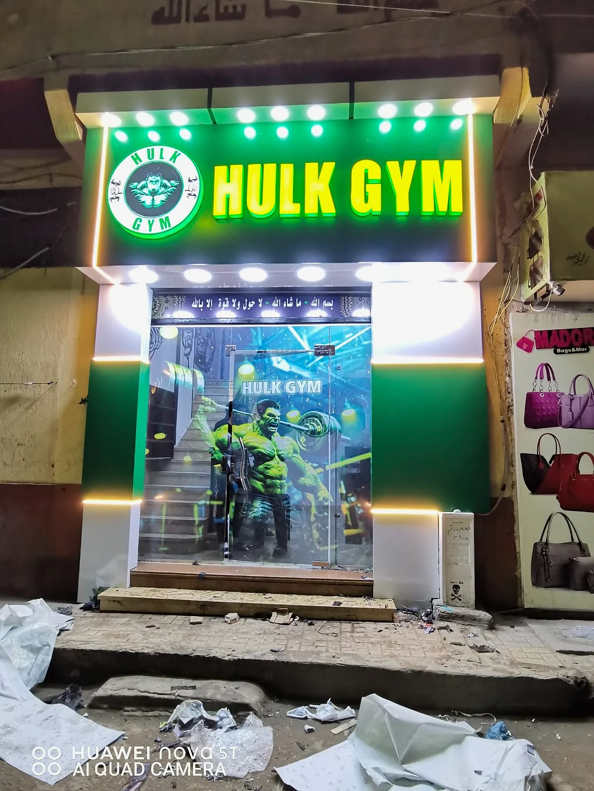 HULK GYM — واجهة جيم بكسوة خضراء وبيضاء وحروف مضيئة، مع طباعة كاملة على الأبواب الزجاجية وإضاءة خطية. من تنفيذ أبو الخير