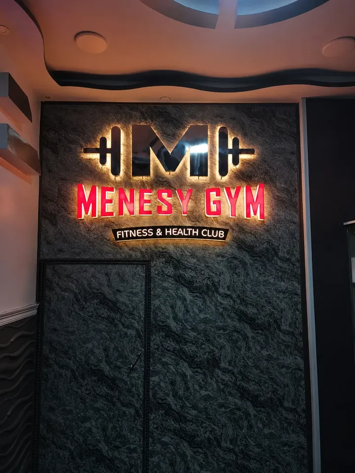 MENESY GYM — شعار وحروف بارزة بإضاءة خلفية مثبتة على كسوة حجرية داخلية. من تنفيذ أبو الخير